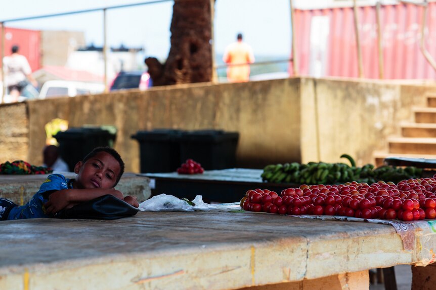A young Tongan boy looks up from resting his head on a stall at local markets.