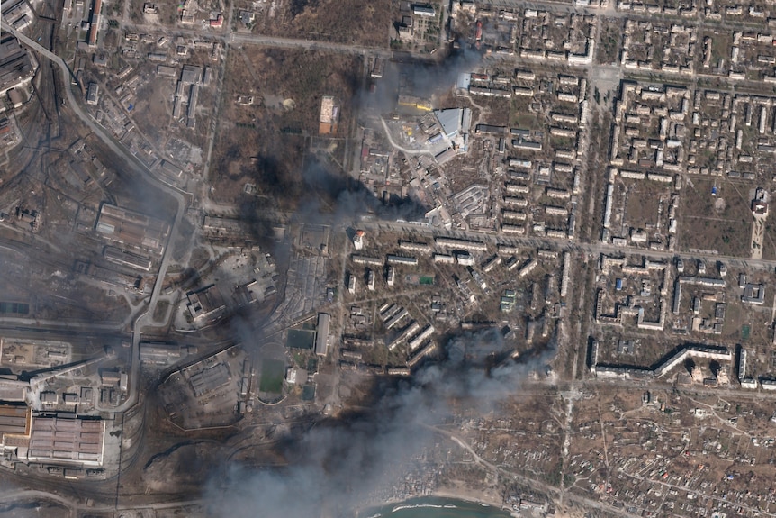 A satellite photo shows multiple civilian buildings burnings, with huge columns of grey smoke covering large parts of the city.