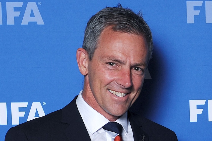 A man in a suit and tie poses for cameras in front of a blue background