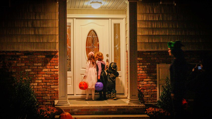 Three small children ringing a doorbell at night