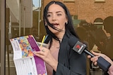 A woman with a drink and book speaks to media outside a courthouse