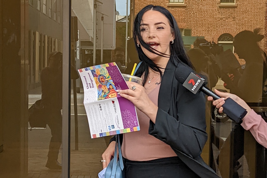 A woman with a drink and book speaks to media outside a courthouse