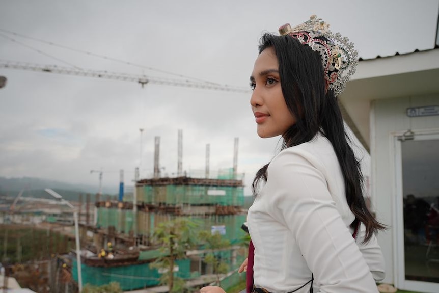 Woman stands on building looking out at a vast construction site.