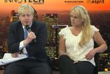 Boris Johnson talks into a microphone as Jennifer Arcuri looks on.