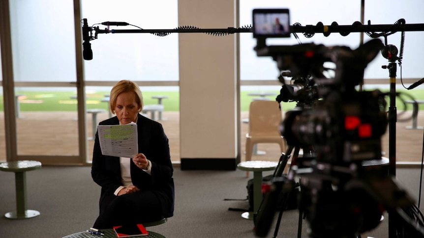 Ferguson sitting in front of camera and microphone looking at sheet of paper with questions written on it.