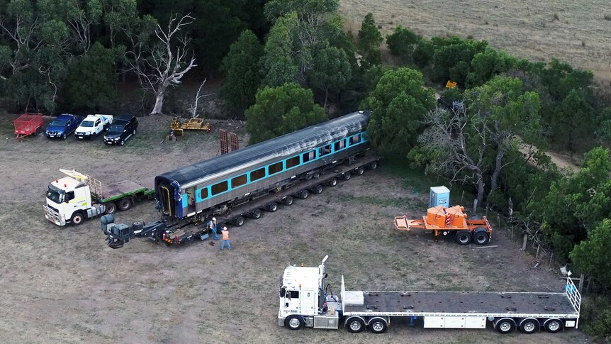 A train carriage is loaded on to a flatbed truck near trees and cars at Wallan.