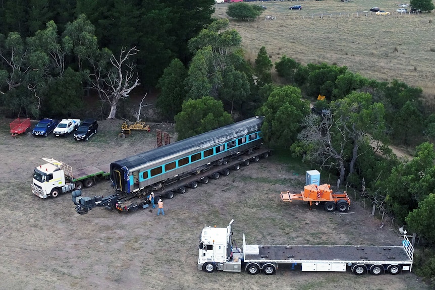 A train carriage is loaded on to a flatbed truck near trees and cars at Wallan.