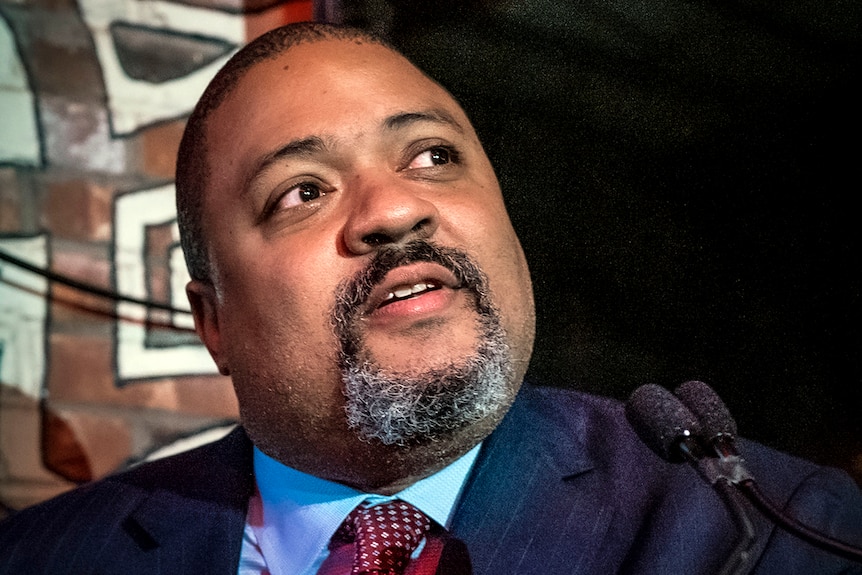 A close up of an unsmiling Alvin Bragg, a bald, dark-skinned man with a close, greying beard.