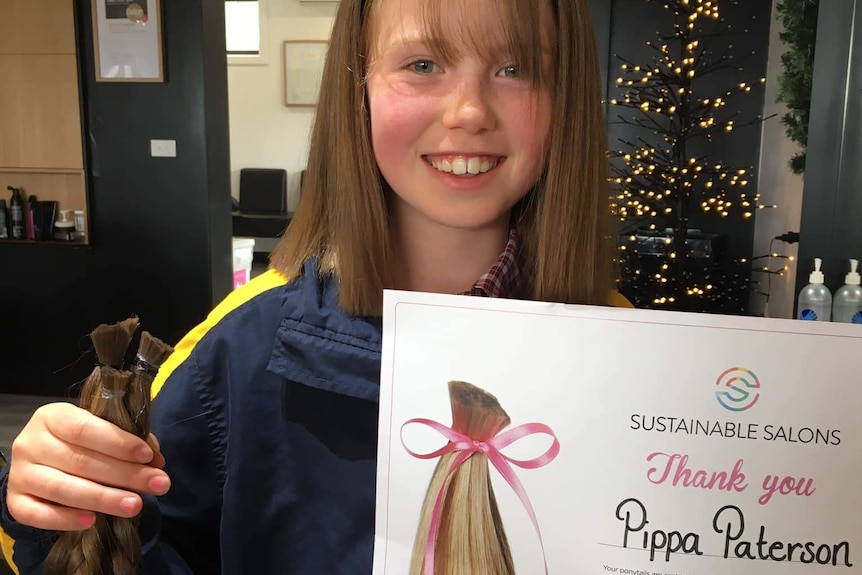 girl holding snipped plaits and a certificate