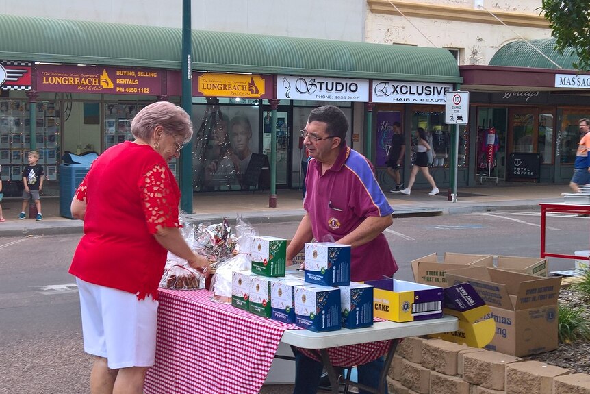 A man in a maroon Lions shirt sells a Christmas cake to a lady wearing red.