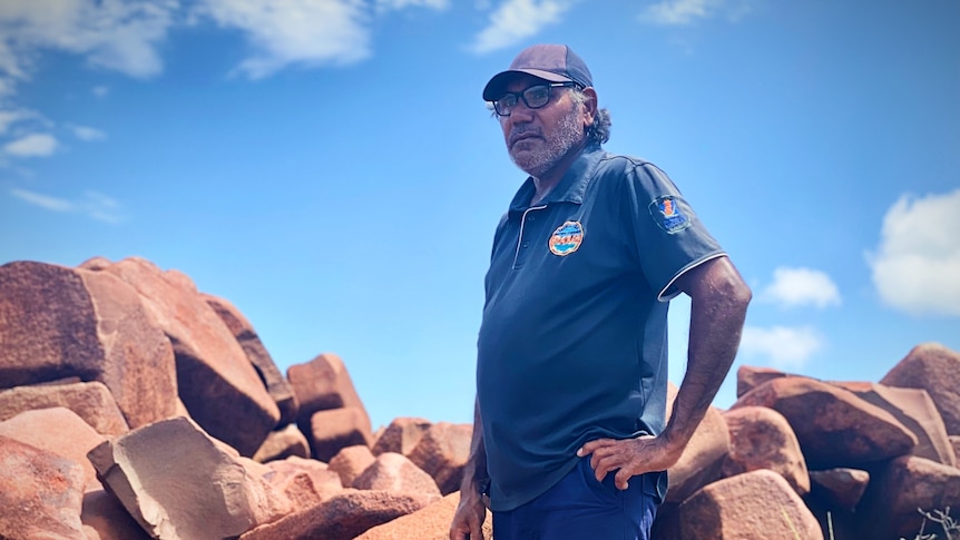 A man standing in front of ancient rocks in Murujuga.