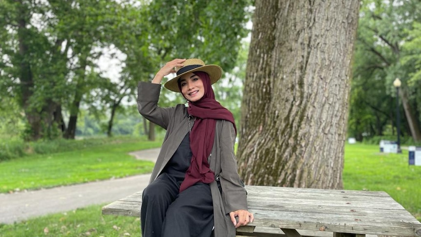 Seorang wanita mengenakan helm dan topi duduk di meja di taman