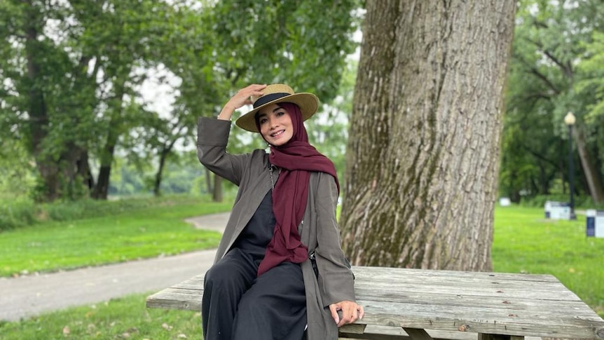 A woman wearing a headscarf and hat sits on a table in a park