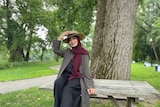 A woman wearing a headscarf and hat sits on a table in a park
