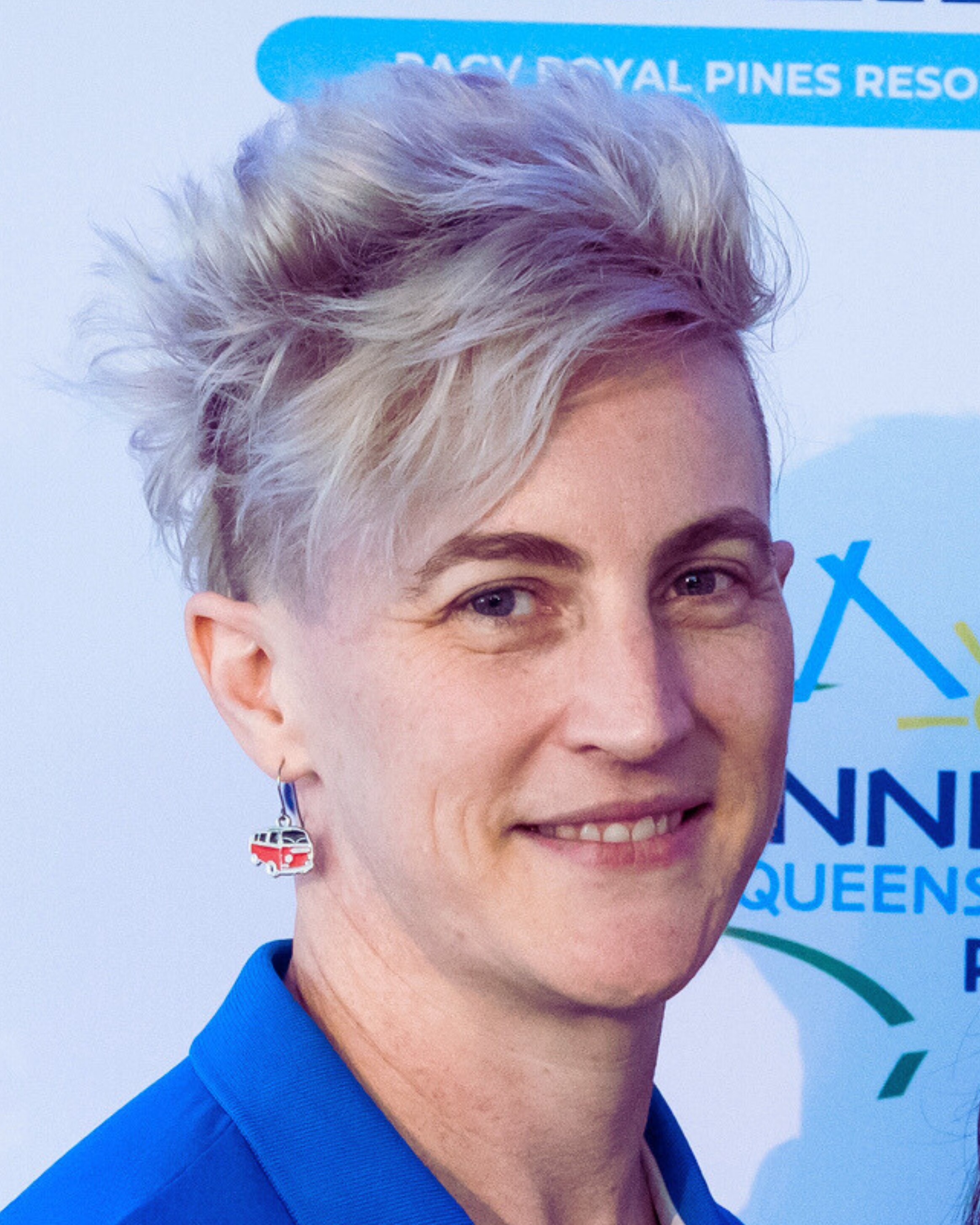 Uma mulher com cabelo prateado curto sorri diante de um fundo de marca.