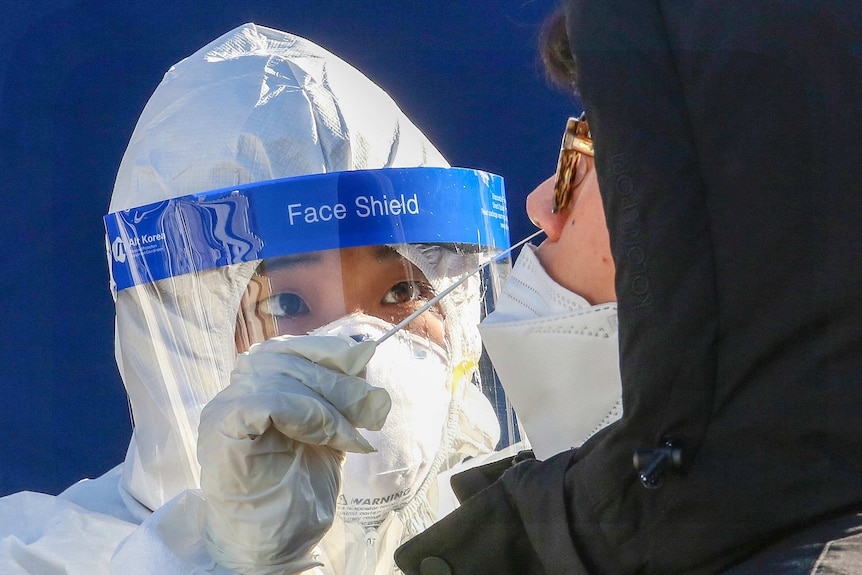 A health worker in full PPE taking a swab of a man's nose