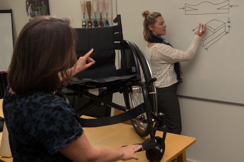 Larissa Burke and Kylie Mines plan adjustments to a wheelchair