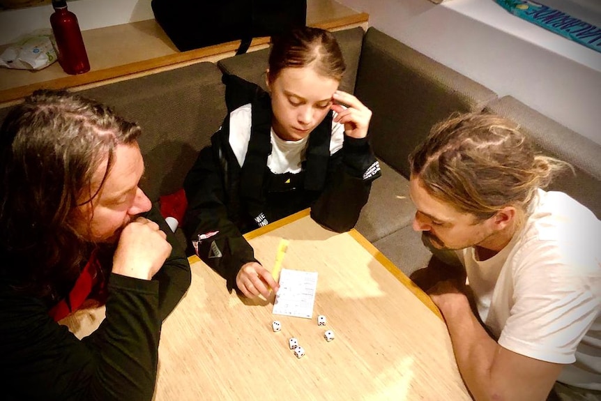 A girl and two men play a dice game in the hull of a boat.