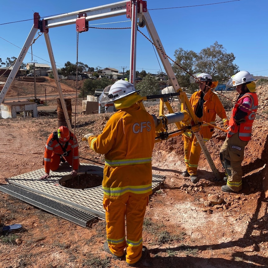 SES volunteers in orange outfits stands around a hole with a frame above it