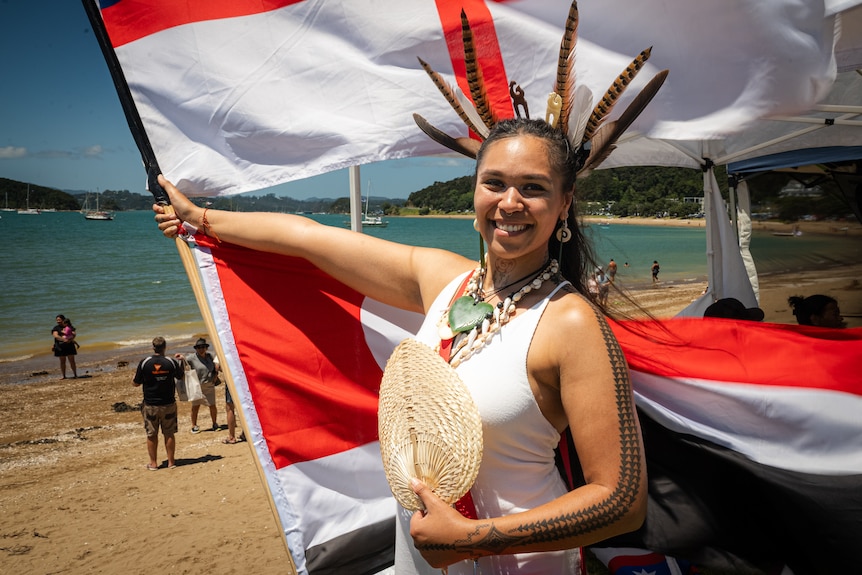 A smiling woman holds up two flags and a woven fan in front of her chest