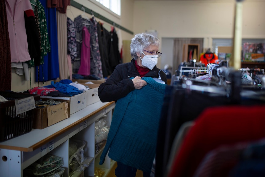 A woman wearing a face mask puts a jacket on a rack in a shop.
