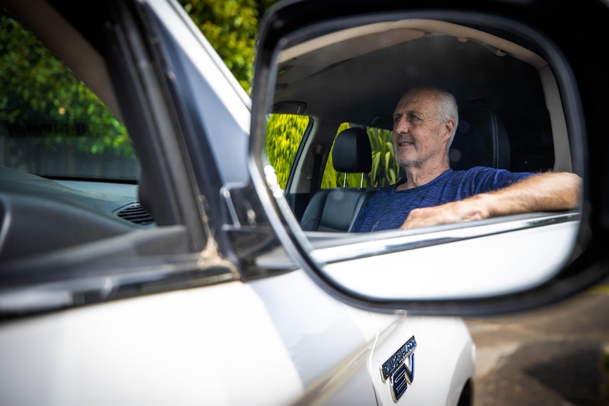 The reflection of a middle aged man is visible in the side mirror of an electric car