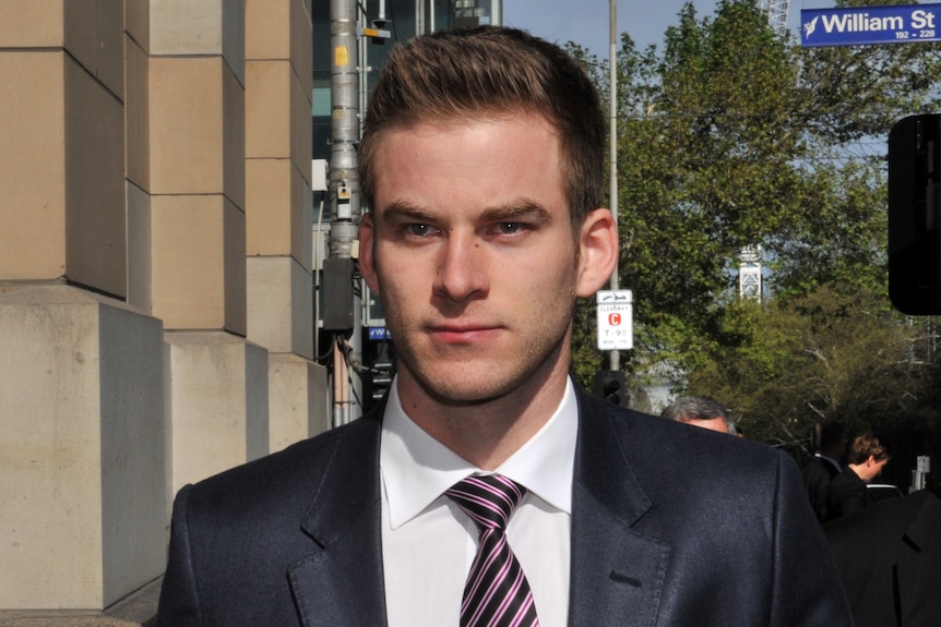 A man in his 20s wears a suit walking down the street