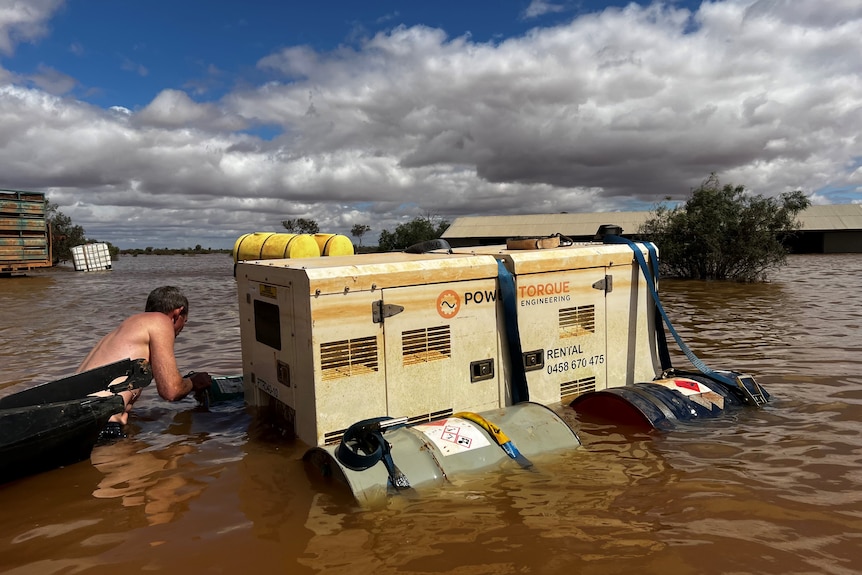 A man in floodwaters working to salvage a generator.  