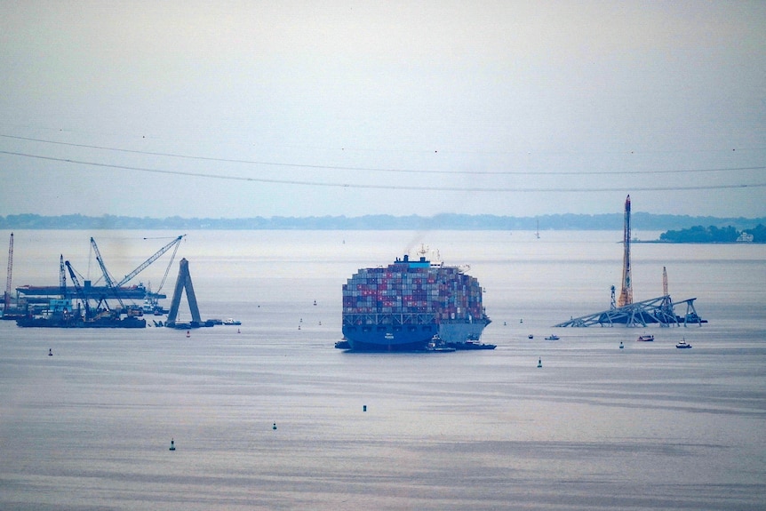 A view from far away of a large cargo ship in the water with metal beams and cranes near it