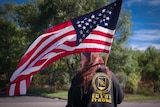 A woman holding a US flag stands with her back to the camera, her jacket with 'Union Strong' written across it 