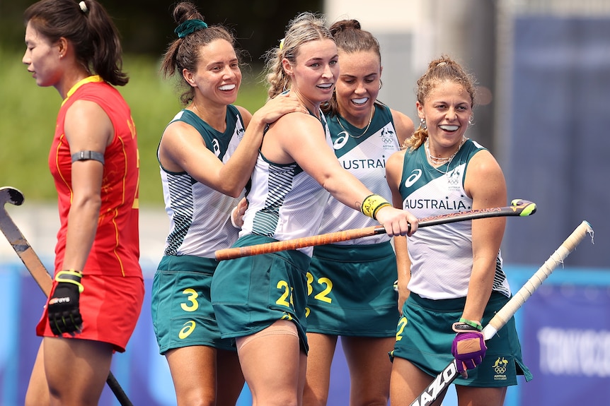 A group of women embrace holding onto hockey sticks