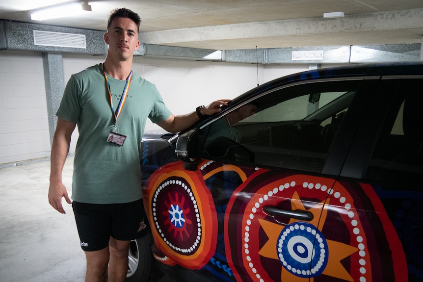 man standing next to police car with Indigenous art decal