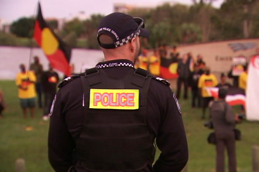 A police officer watches protesters outside Carrara Stadium ahead of the Commonwealth Games Opening Ceremony.