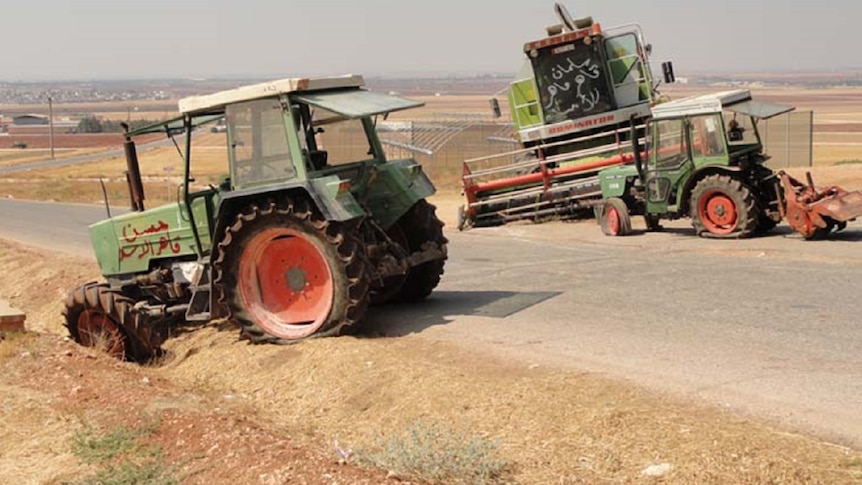 Tractors with graffiti and busted tyres sit derelict on the road side in Syria with untended brown fields behind