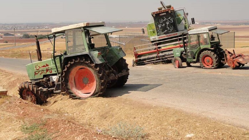 Tractors with graffiti and busted tyres sit derelict on the roadside in Syria with untended brown fields behind