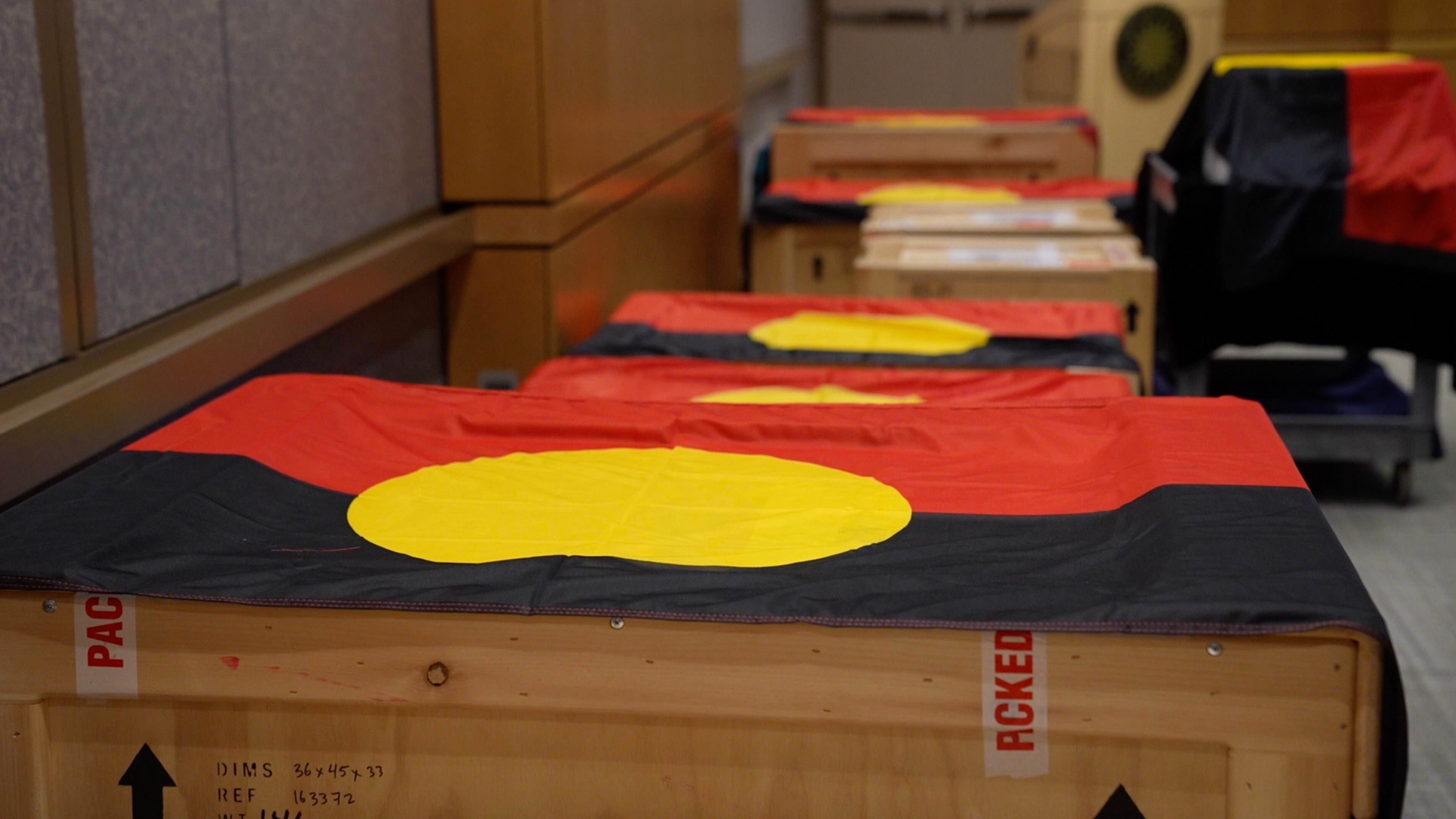 Packing crates with black, yellow and red Aboriginal flags draped over them