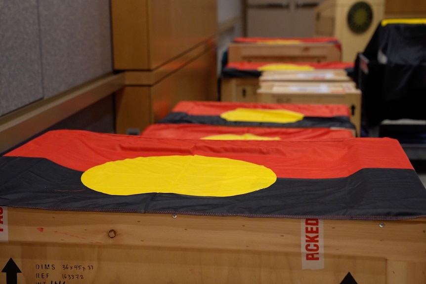 Packing crates with black, yellow and red Aboriginal flags draped over them