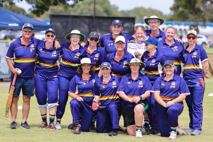 A team of female cricketers and their coaches in blue and rainbow jerseys.