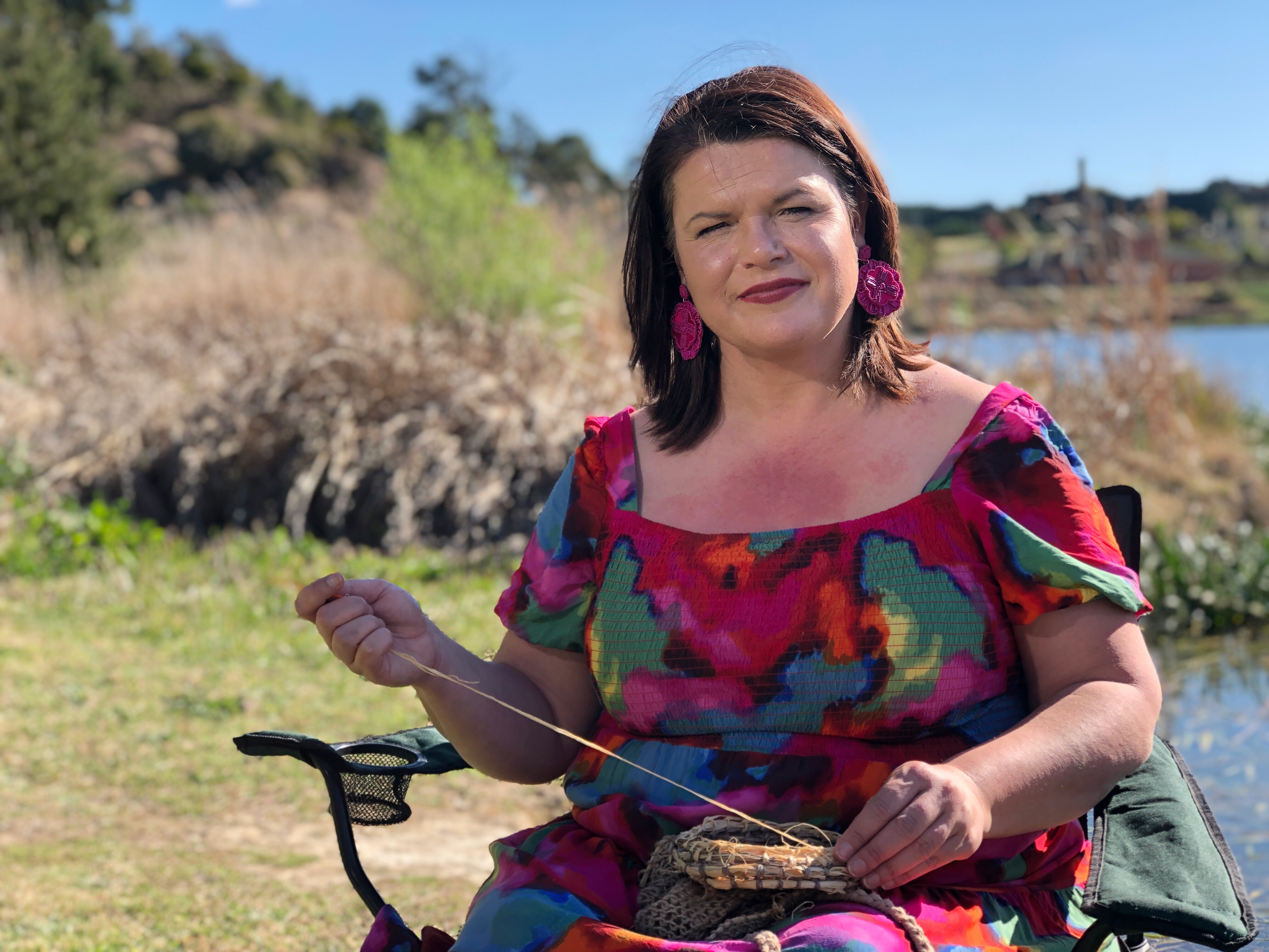 Woman wearing colourful dress sitting beside a river. 