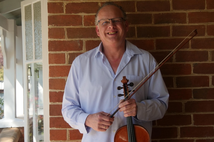 A man smiles holding a viola
