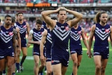 Nathan Fyfe leads a group of Fremantle Dockers players off the field with his hands on his head.