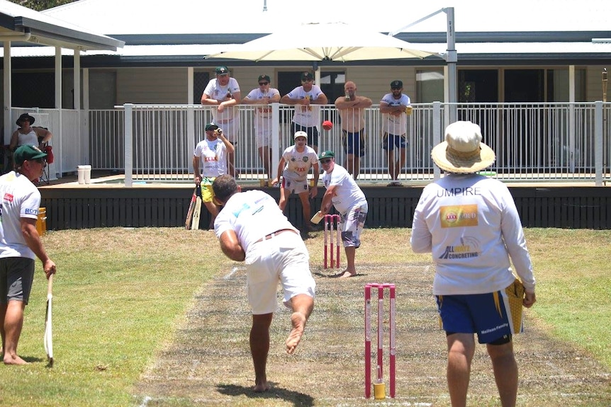 A game of cricket at a backyard, the pitch looking a little brown and worse for wear.