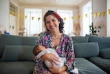 Mum smiling on the couch while holding newborn