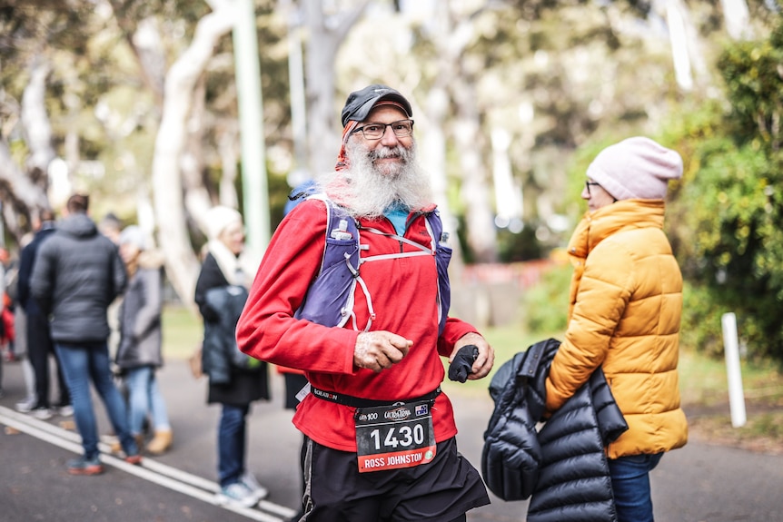 An elderly man in a red jacking running and smiling.