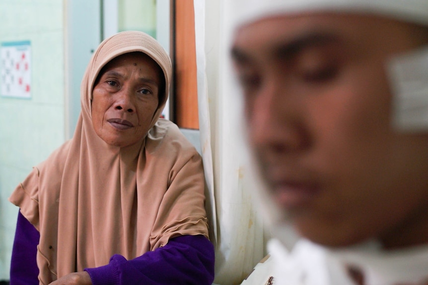 A woman sits beside her son in hospital