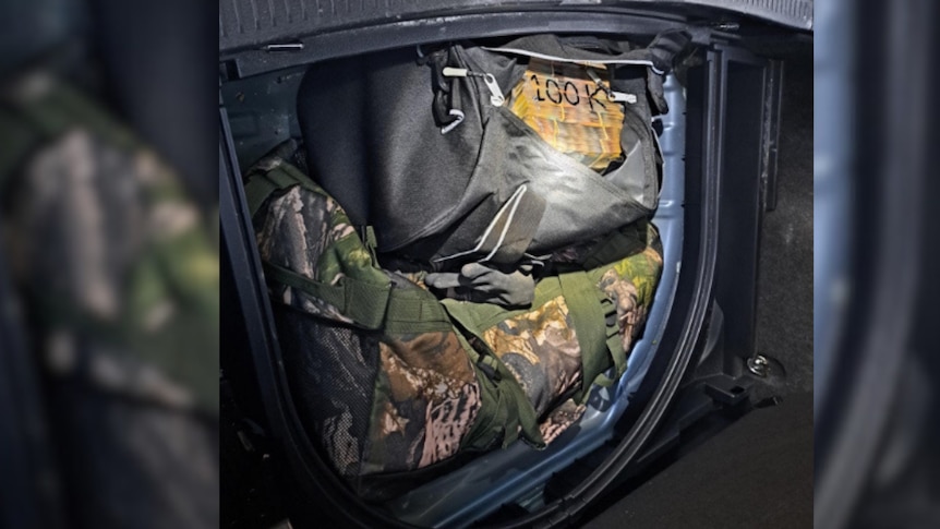 Two duffel bags are seen in a car boot, containing $100 bills packed in vacuum bags. 100K is written on one bag.