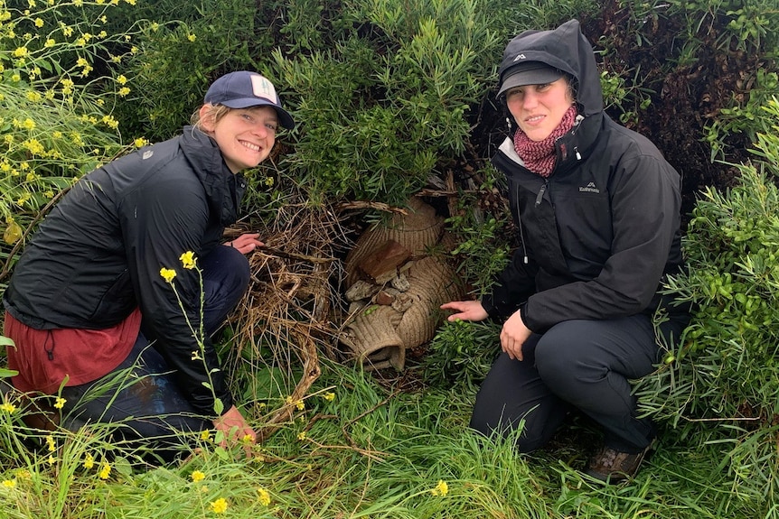 Two women in wet weather gear in green habitat with a ceramic nesting burrow between them