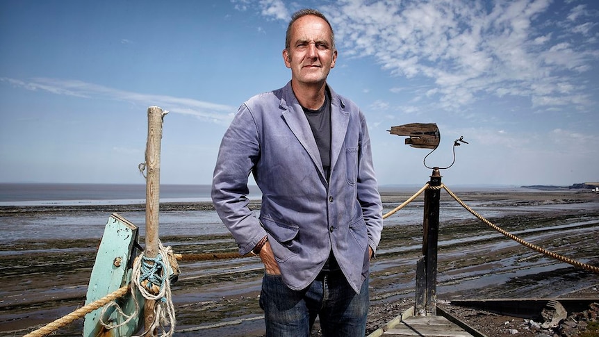 Kevin McCloud poses on the seaside in front of the ocean
