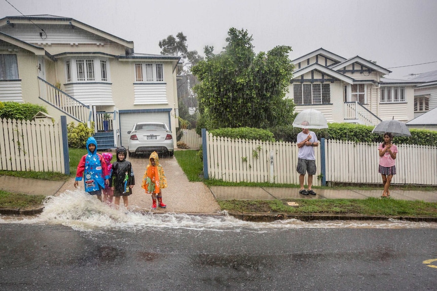 A family plays in the rain outside a home from ex-cyclone Debbie in Newmarket.