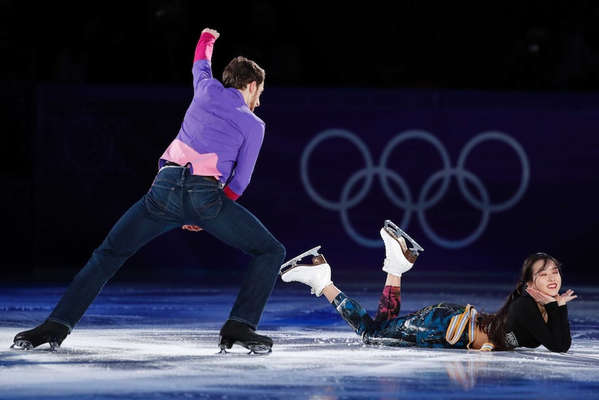 Yura Min lies on the ice with her feet in the air as Alexander Gamelin skates around her.